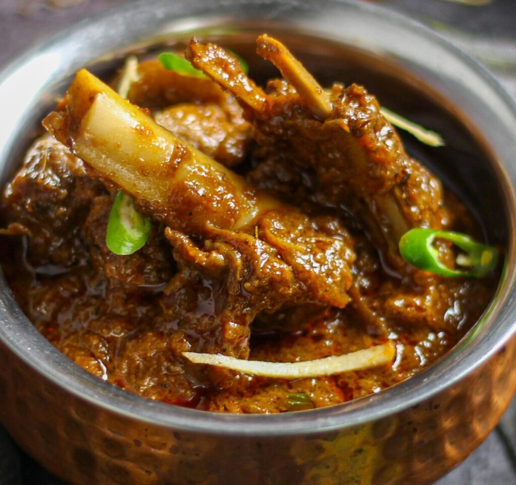 Close-up of a spicy mutton curry served in a traditional copper bowl, showcasing rich Indian flavors.
